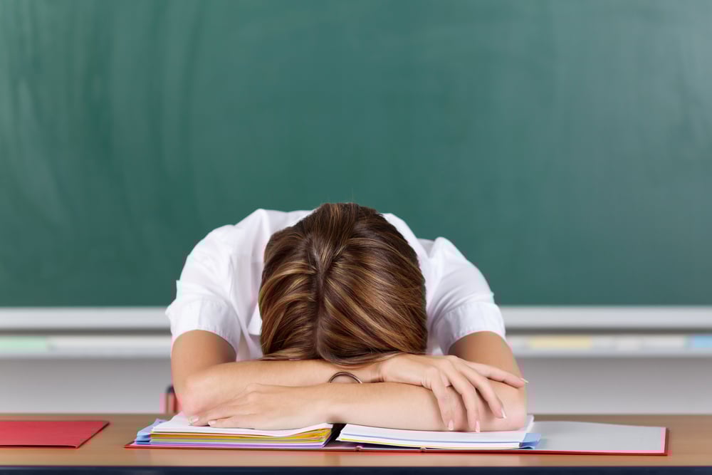 Stressed student with their head down on their textbooks in classroom.