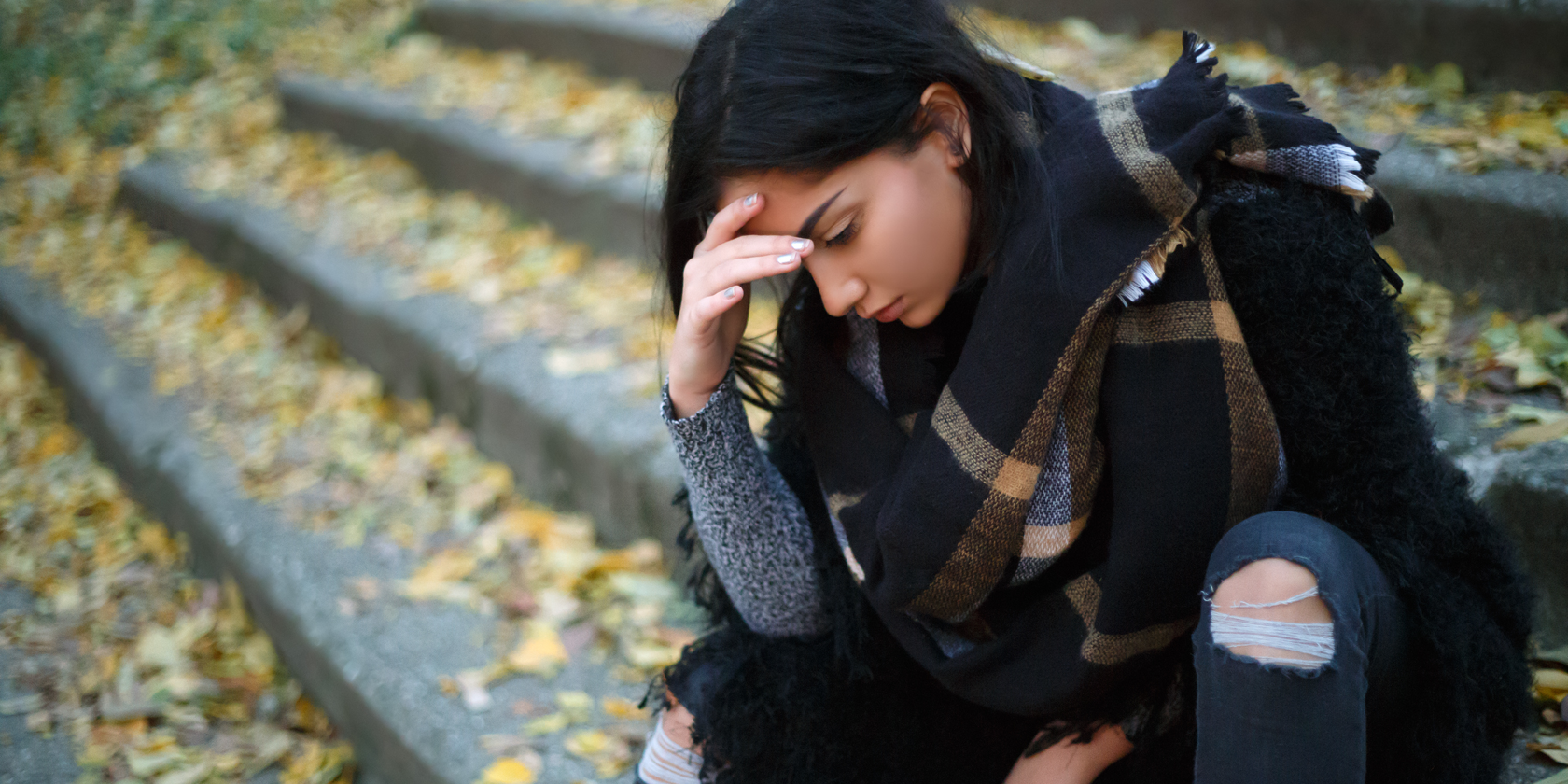 Girl with head down and hands by her temples in a moment of deep reflection.